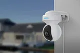 KAAMERAMAAILM.EE - A Valvekaamera Reolink E1 Outdoor Dual Band WiFi-ga 5MP, PTZ, 3X Zoom ning isiku ja sõiduki tuvastusega on paigaldatud välisseinale, taustal hägusad hooned ja veekogu. (2/2)
