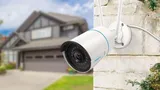 KAAMERAMAAILM.EE - Valge Reolink RLC-510WA 5MP Dual Band WiFi valvekaamera isiku ja sõiduki tuvastusega on paigaldatud välisseinale, taustal on hägustatud eeslinna maja ja garaaž, et suurendada turval (2/5)