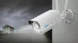KAAMERAMAAILM.EE - Valvekaamera Reolink RLC-511WA 5MP Dual Band WiFi 5-kordse suumiga on paigaldatud välisseinale, jälgides õueala, mille taustal on näha hägune maja ja pilvine taevas, mis viitab akti (1/5)