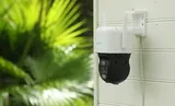 KAAMERAMAAILM.EE - Valvekaamera Reolink TrackMix WiFi kahe objektiiviga 8MP, PTZ, 6X Zoom, isiku ja sõiduki tuvastusega ning jälgimisega on paigaldatud seinale; taustal on nähtavad rohelised taimed ja (3/3)